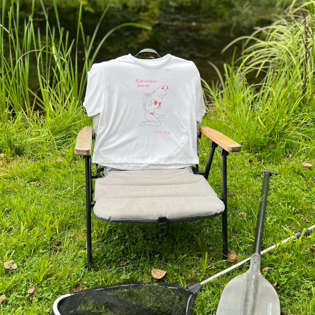 Sirena Fish Woman crop top in white, draped over a camp chair beside a pond with a fishing net