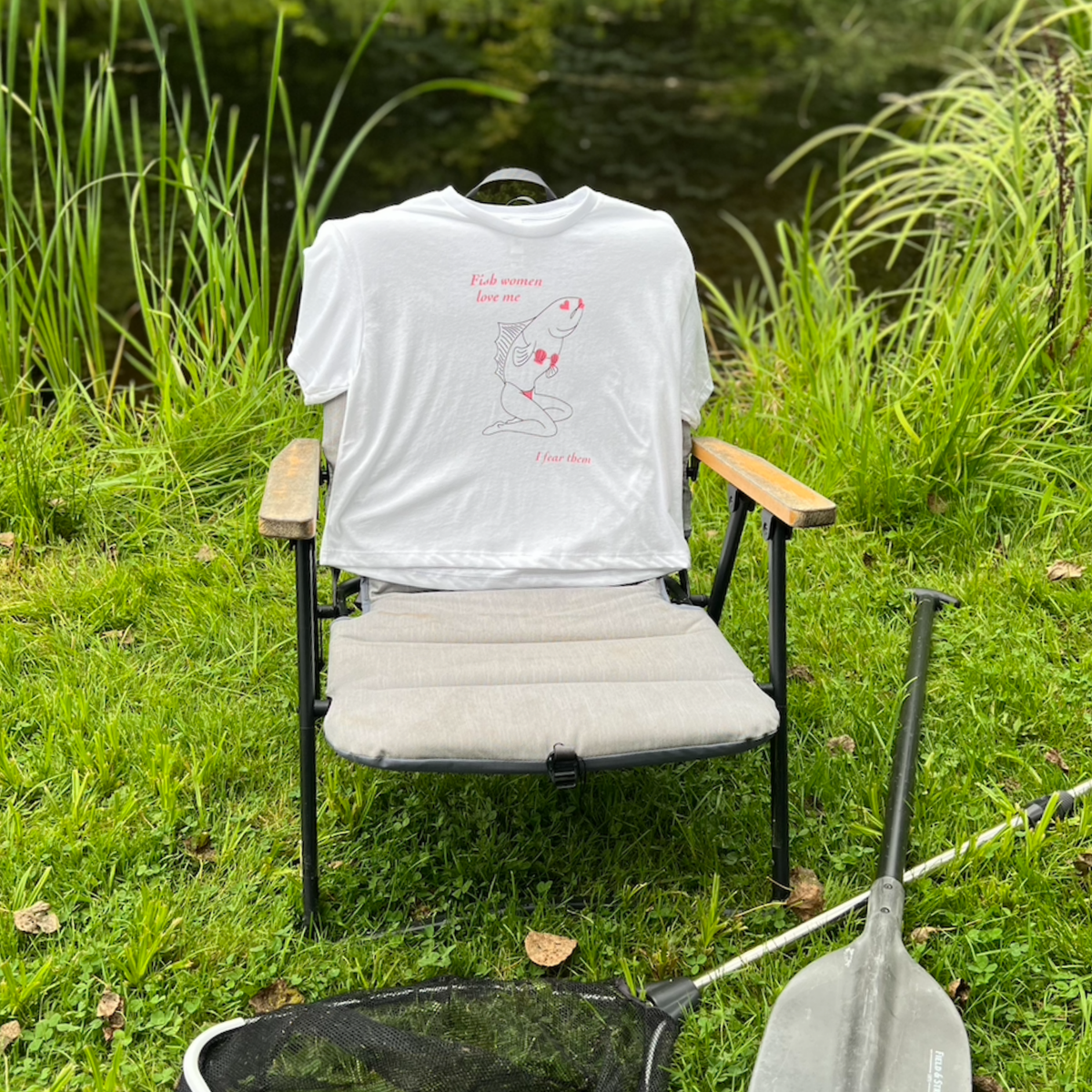 Sirena Fish Woman crop top in white, draped over a camp chair beside a pond with a fishing net