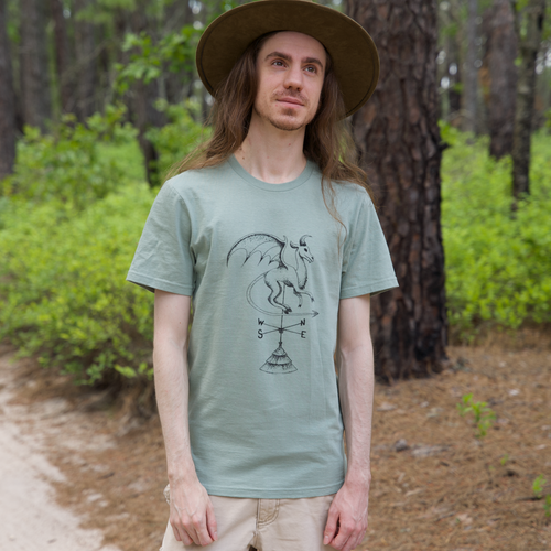 Model wearing Batsto (Jersey Devil) T-Shirt from Cryptid Records in sage green, outdoors in a pine forest
