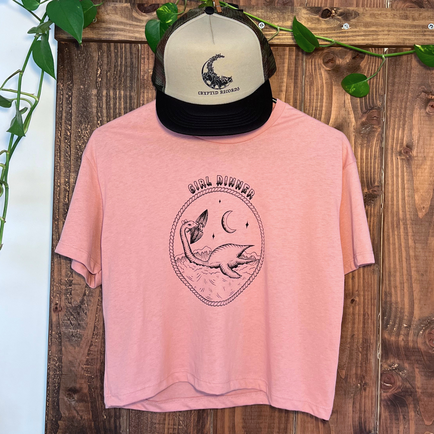 Plesia Girl Dinner crop top in desert pink from Cryptid Records, shown with a pink trucker hat