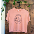 Plesia Girl Dinner crop top in desert pink from Cryptid Records, shown with a trucker hat