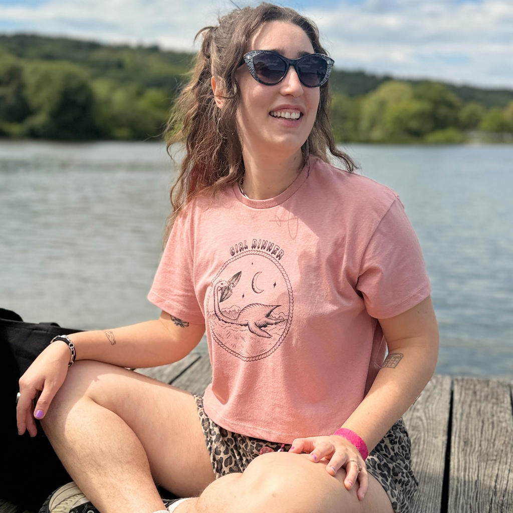Model wearing Plesia Girl Dinner crop top in desert pink from Cryptid Records, seated